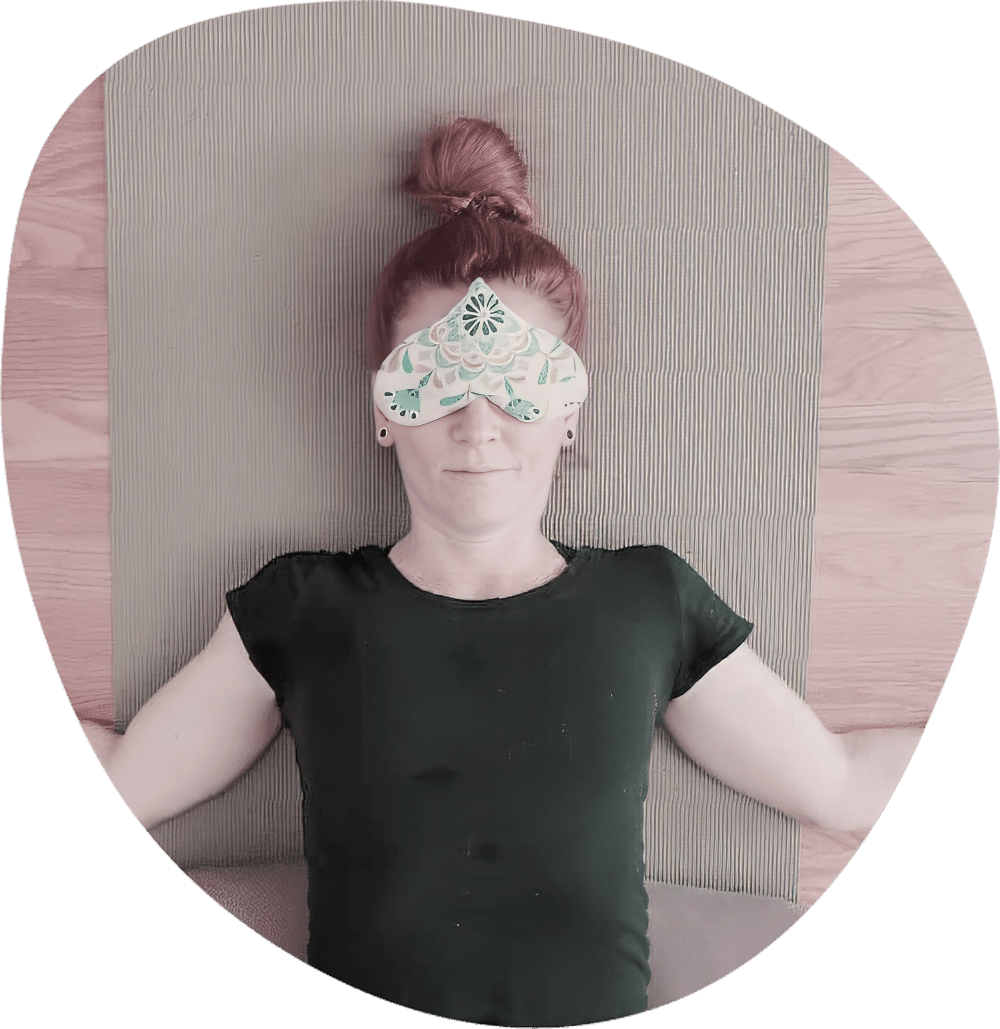 Student in savasana resting on a yoga mat with an eye pillo